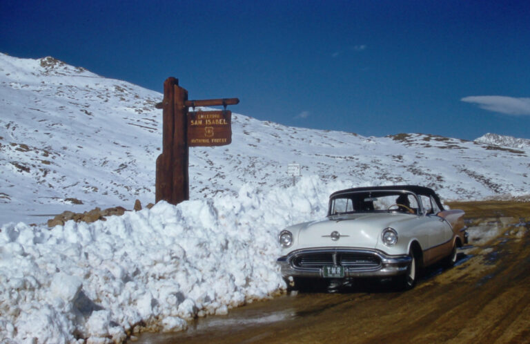 1956 Oldsmobile 98 in orange near Aspen, Colorado in spring time with melting snow in year 1961